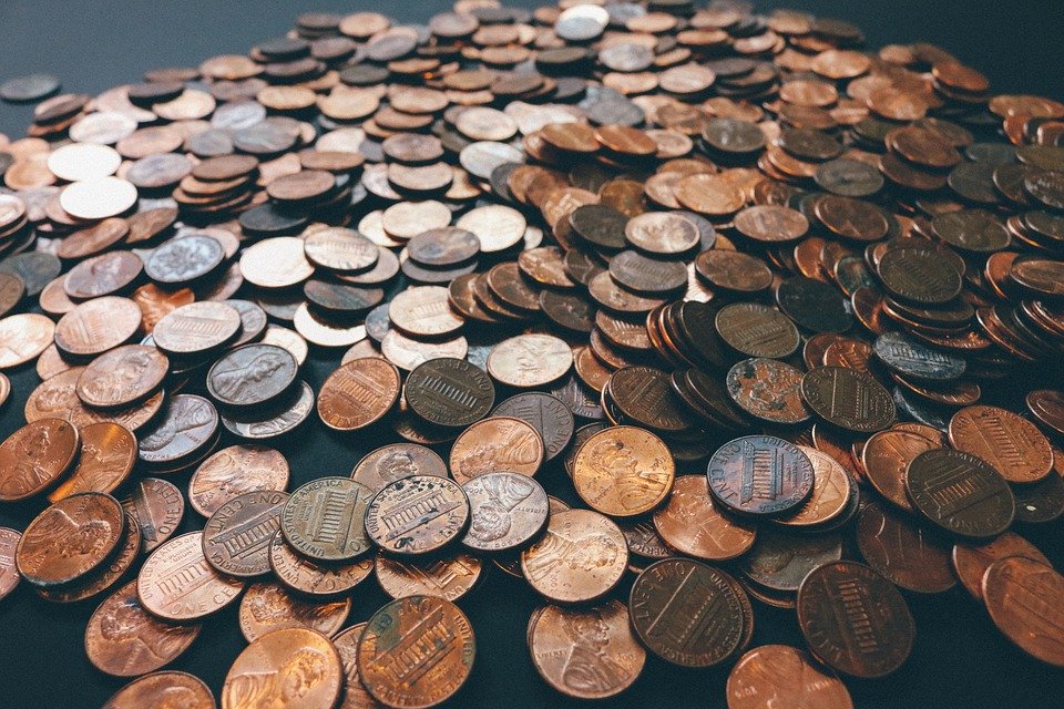 A large pile of scattered pennies and other small coins on a dark surface.