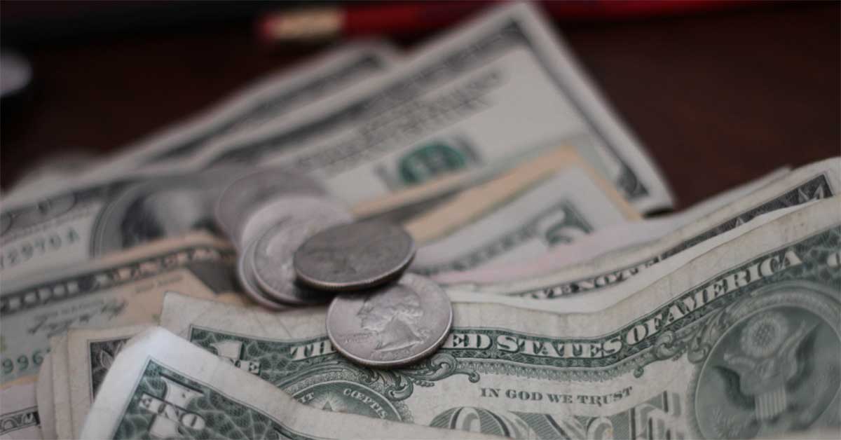 A close-up image of various U.S. dollar bills and coins scattered on a surface, capturing the essence of financial wellness. The bills include denominations of one and ten dollars, while the coins appear to be quarters. The background is slightly blurred, emphasizing the money in the foreground.