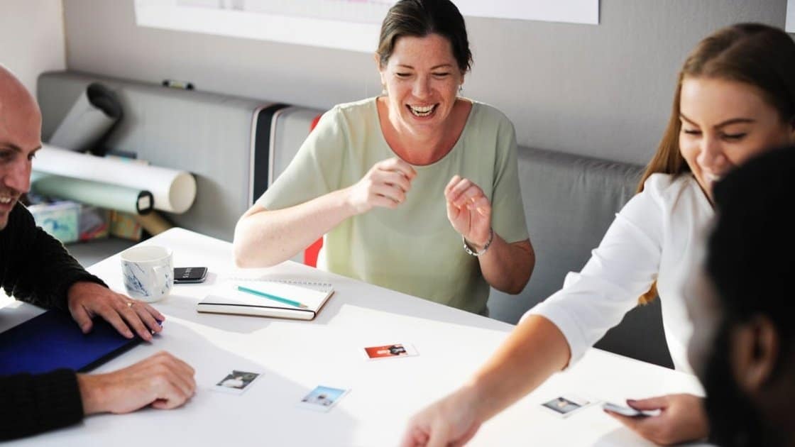 Four people sit around a table sharing laughs while looking at photographs and papers.