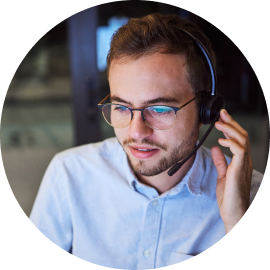 Man wearing glasses and a headset, looking down and smiling slightly, with a blurred background.