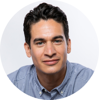A man with short, dark hair wearing a blue checked shirt, looking towards the camera against a plain white background.