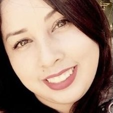 Person smiling with long dark hair, outdoors in bright sunlight.